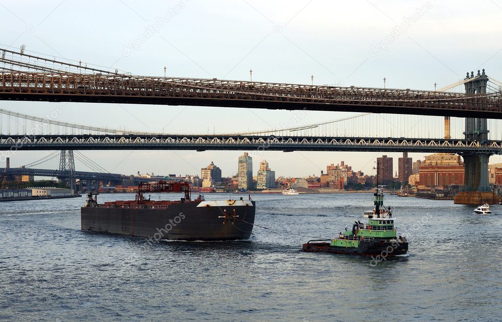 A tugboat pulls a container ship passed the Brooklyn Bridge