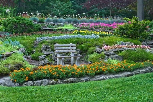 Banco de madera en jardín de verano con flores en flor — Foto de Stock