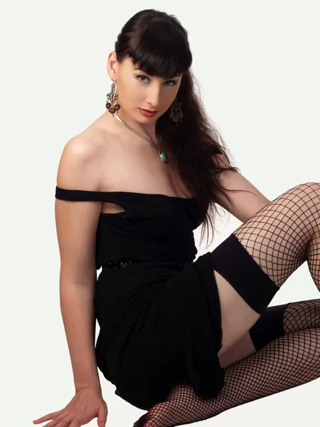 Woman in black dress and fishnet stockings sitting — Stock Photo, Image