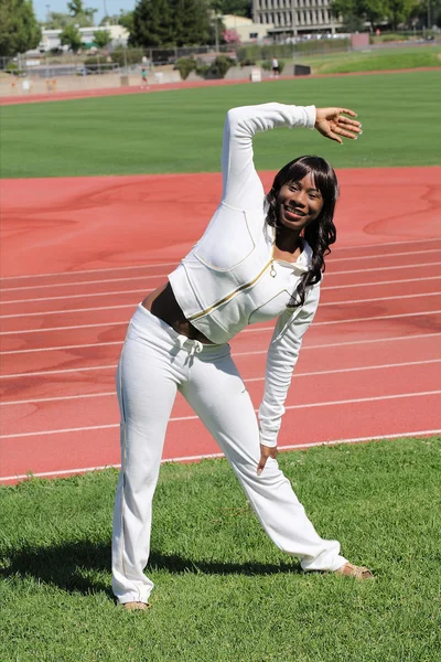 Young black woman stretching at track on grass — Stock Photo, Image