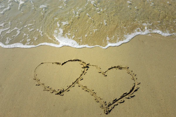 Два сердца, нарисованные на пляже на закате — стоковое фото
