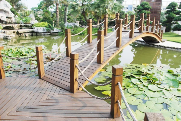 Η γέφυρα του σκάφους ξύλου σε έναν κήπο νερού λιμνών στην Κίνα ένα τροπικό θέρετρο. — Φωτογραφία Αρχείου