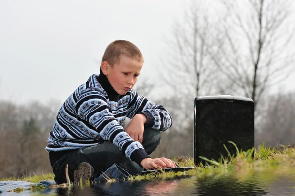 Pojke med anteckningsboken sitter nära vatten — Stockfoto