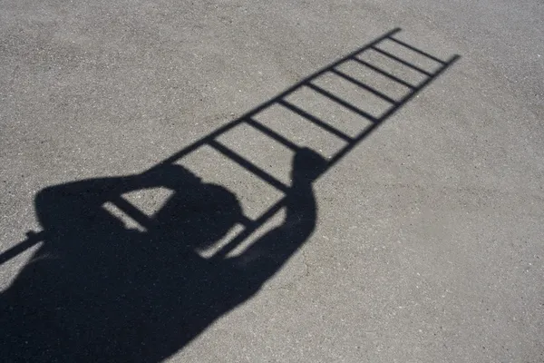 Sombra de homem escalando escada no asfalto — Fotografia de Stock