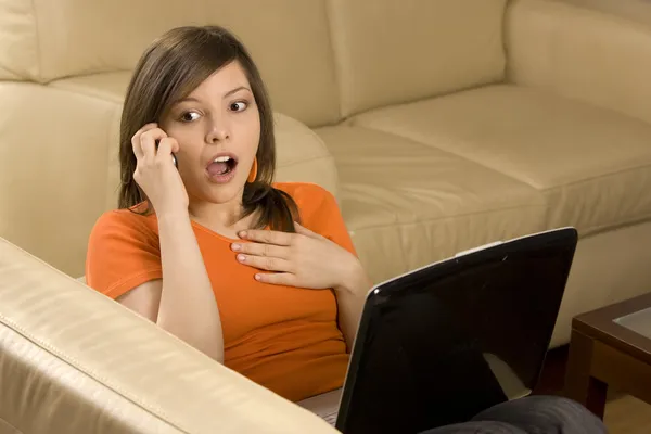Förvånad ung kvinna med laptop och mobiltelefon — Stockfoto