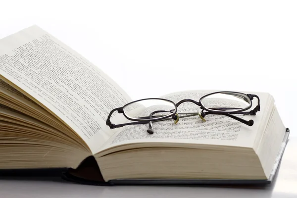 Открытая книга с очками — стоковое фото