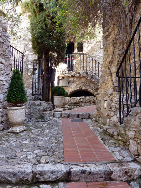 Red pavement, stairs with fences and walls of houses in a street of historical Eze village in south France