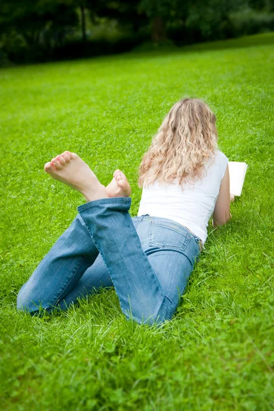 Молодая кудрявая блондинка читает книгу в парке — стоковое фото