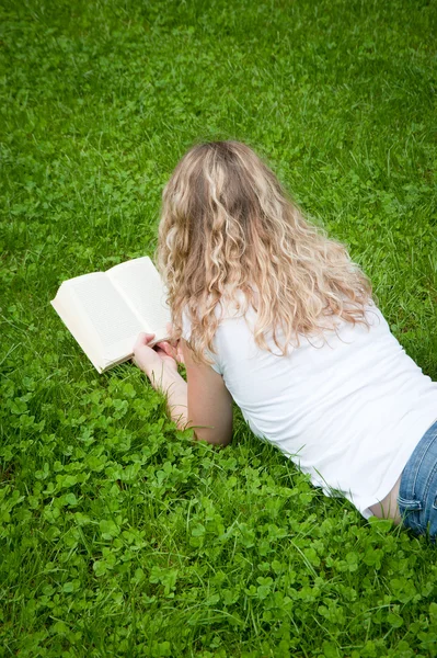 Jovem loira encaracolada lendo um livro em um parque — Fotografia de Stock