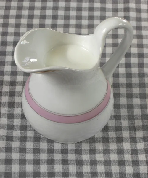 Ancient cream-jug on a checkered cloth — Stock Photo, Image