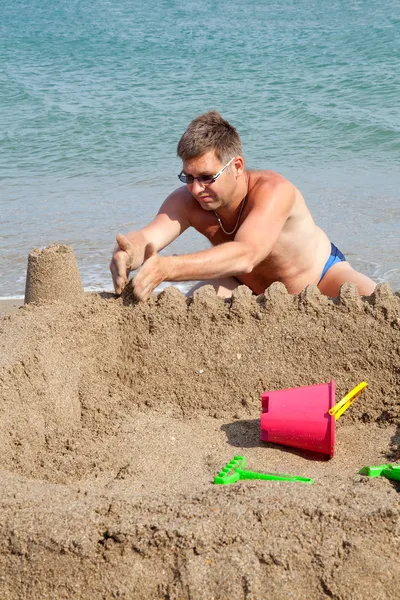 Homem está fazendo castelo de areia na praia — Fotografia de Stock