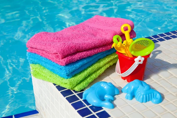 Handdoeken en plastic speelgoed in de buurt van het zwembad zwemmen — Stockfoto