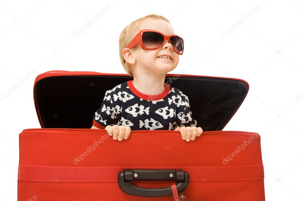 Little kid in sunglasses looking out red suitcase