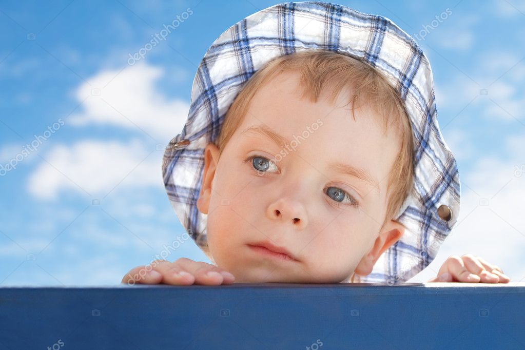 Sad cute little boy in hat on sky background