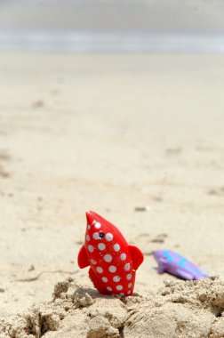 Red fish toy on beach clipart