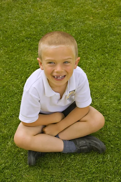 Bonito menino de escola de seis sete anos sentado na grama — Fotografia de Stock