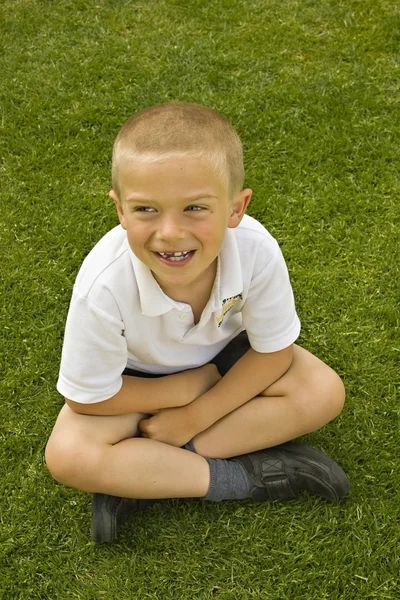 Bonito menino de escola de seis sete anos sentado na grama — Fotografia de Stock