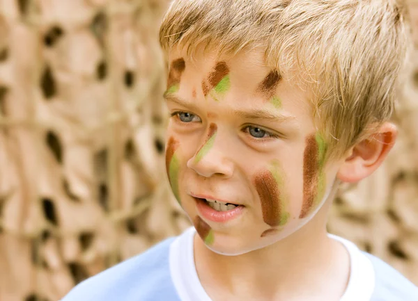 En ung pojke med kamouflage färg i ansiktet Stockbild