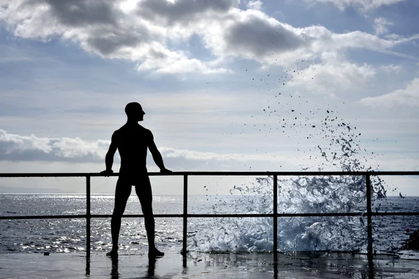 Silhouette of young man standing at the seaside, wave splash — Stock Photo, Image