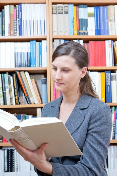 Mujer joven leyendo un libro en la biblioteca — Foto de Stock