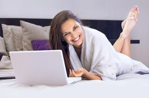 Счастливая дама на кровати с ноутбуком — стоковое фото