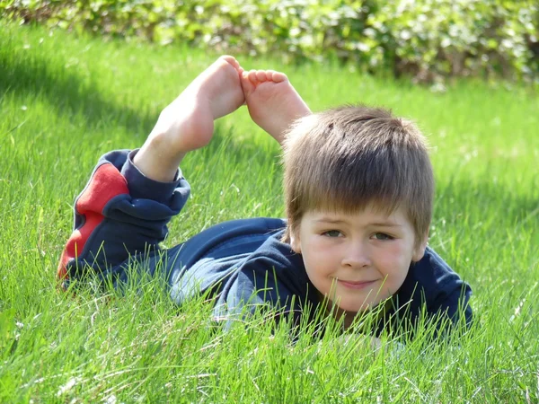 Drengen lå på græsset. - Stock-foto