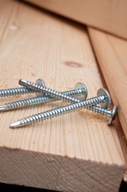 Four steel screws on a wooden plank clipart