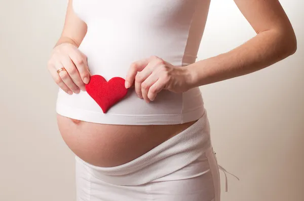 Pregnant woman put a toy heart — Stock Photo, Image