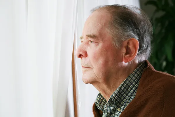 Oudere man kijkt uit raam — Stockfoto