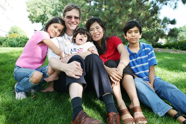 Çimenlerde oturan geniş ırklı bir aile. — Stok fotoğraf