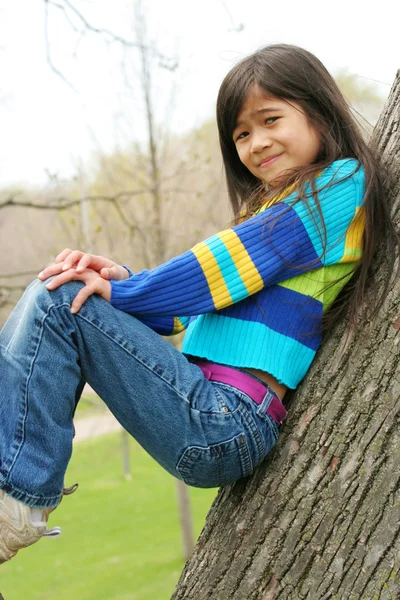 Красивая маленькая девочка сидит на дереве — стоковое фото