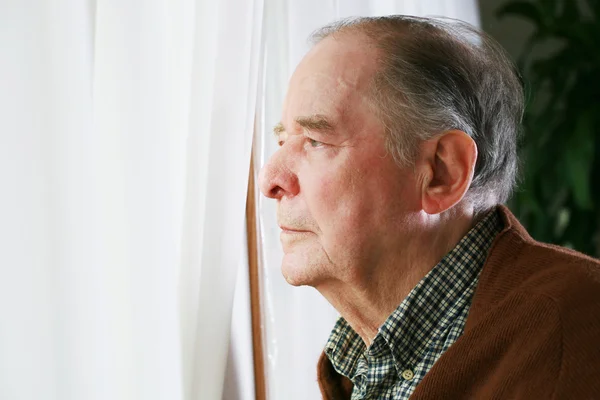 Oudere man kijkt uit raam Rechtenvrije Stockfoto's