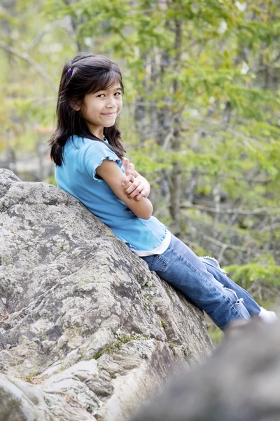 Menina sentada contra a rocha, sorrindo — Fotografia de Stock