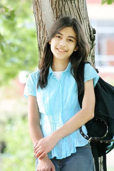 Young teen girl standing with backpack by tree, smiling. Part as — Stock Photo, Image
