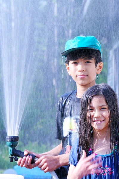 Брат и сестра играют с водяным шлангом — стоковое фото