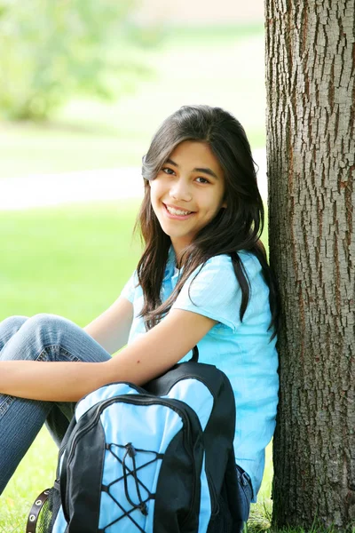Молодая девушка сидит на дереве с рюкзаком — стоковое фото
