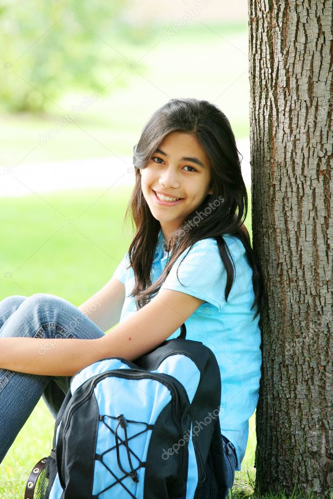Young teen girl sitting against tree with backpack