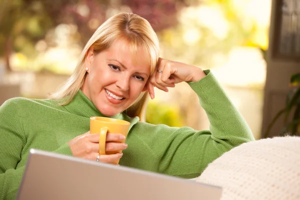 Lachende vrouw met beker met behulp van laptop — Stockfoto