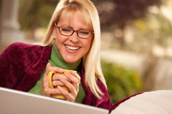 Улыбающаяся женщина с чашкой с помощью ноутбука — стоковое фото