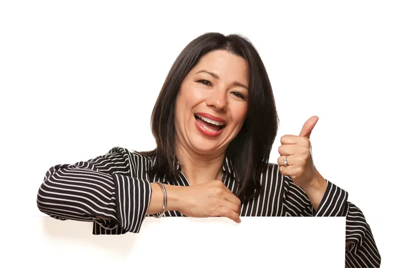 Atrakcyjna kobieta wieloetnicznym uśmiechający się, opierając się na puste biały znak z kciukiem — Zdjęcie stockowe