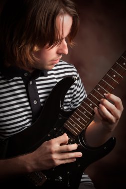 Young Musician Plays His Electric Guitar with Dramatic Lighting. clipart