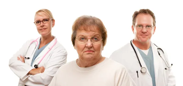 Besorgte Seniorin mit Ärzten im Hintergrund auf weißem Hintergrund. — Stockfoto