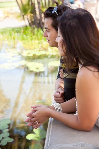 Atractiva pareja hispana pasa por alto estanque juntos al aire libre . — Foto de Stock