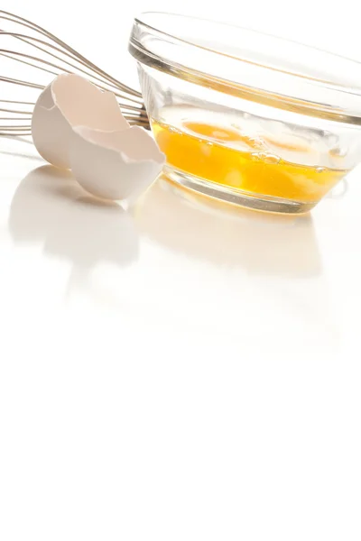 Misturador de mão com ovos em uma tigela de vidro em um fundo branco reflexivo . — Fotografia de Stock