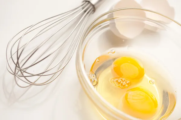Misturador de mão com ovos em uma tigela de vidro em um fundo branco reflexivo . — Fotografia de Stock
