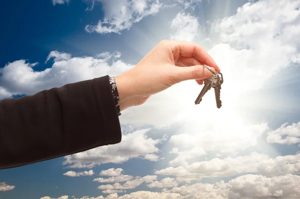 Kvinna håller ut par nycklar över moln och himmel — Stockfoto