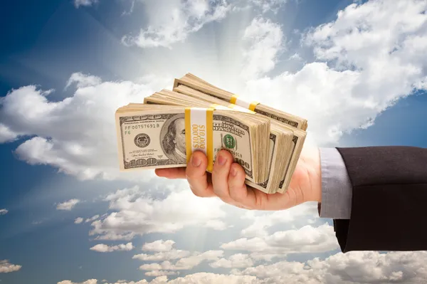 Мужчина держит стопку денег над облаками и небом — стоковое фото