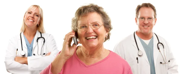 Gelukkig senior vrouw met behulp van de mobiele telefoon en artsen achter — Stockfoto