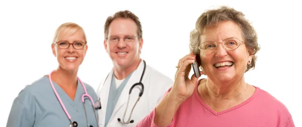 Happy Senior Woman Using Cell Phone and Doctors Behind — Stock Photo, Image
