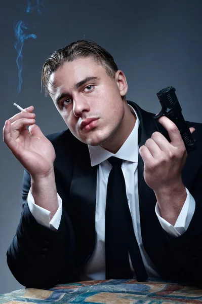 Portrét pohledný mladý gangster s cigaretou a zbraň — Stock fotografie